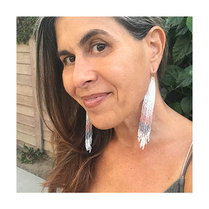 A woman wears long dangling Handmade Seed Bead Fringe Earrings in chevron pattern with white, pink and gray beads.