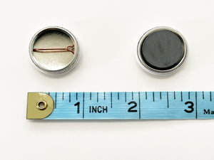 Close up of the backs of pin back button and magnet, shown with measuring tape for size, one inch diameter