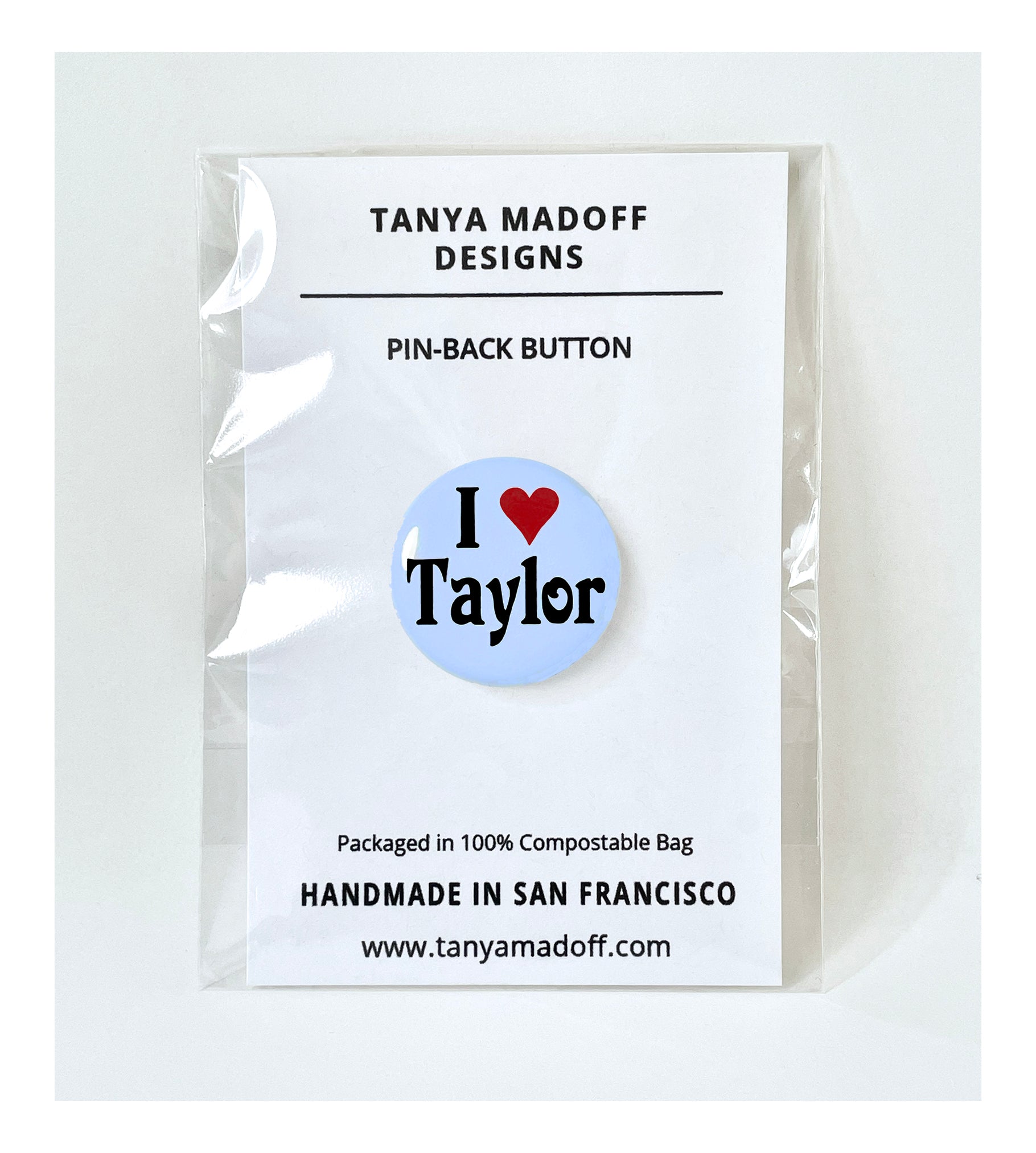 I Love Taylor, 1 inch pin back button, in honor of Taylor Swift, with black lettering and red heart on pale blue background, packaged on recycled paper, in 100% compostable clear glassine bag