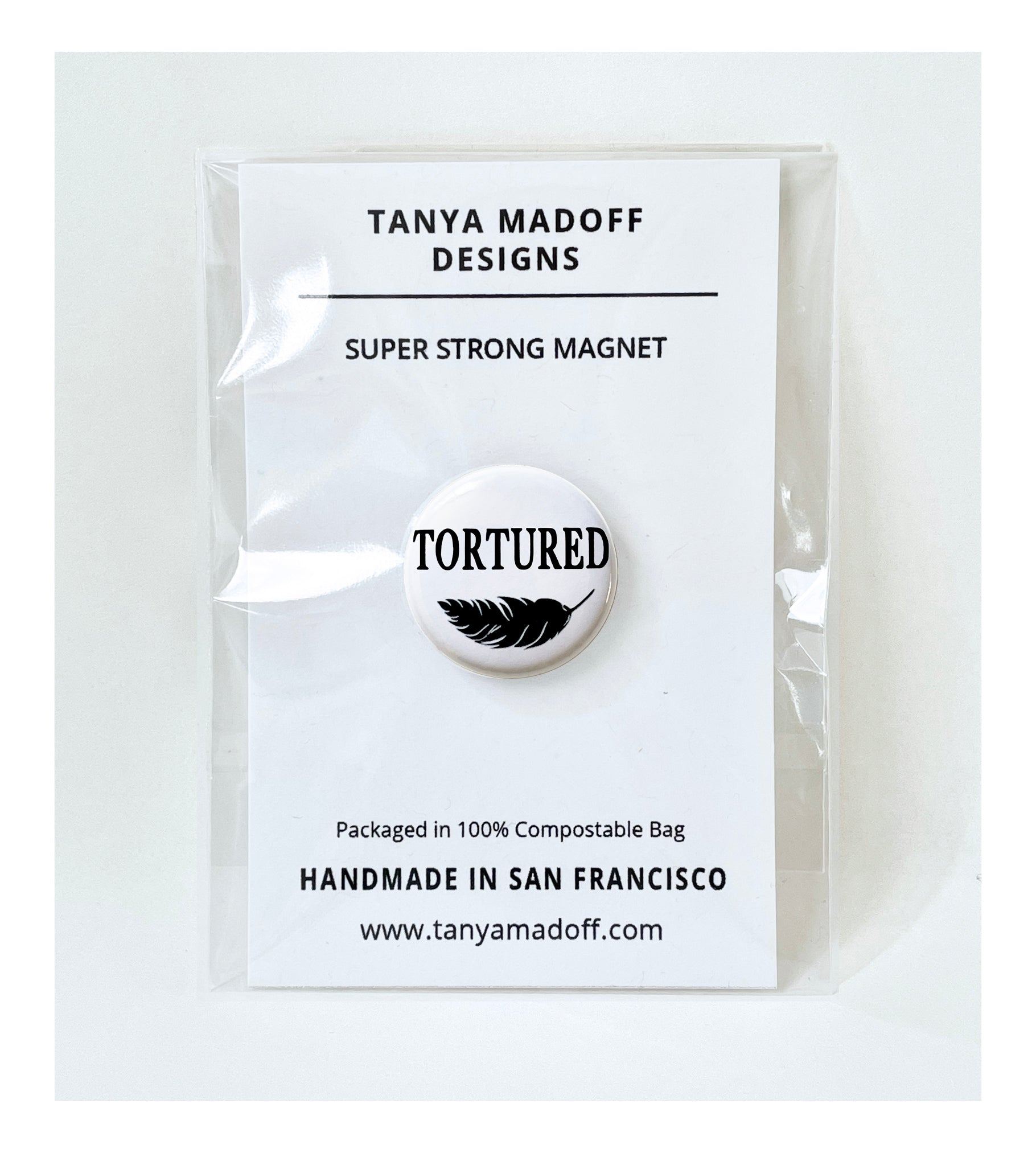 Tortured, 1" extra strength magnet, in honor of Taylor Swift's album, The Tortured Poets Department, black lettering and feather drawing on white background, packaged on recycled paper, in 100% compostable clear glassine bag